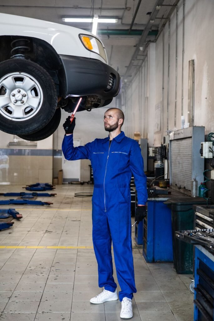 Service technician in coveralls working underneath a commercial vehicle in a repair shop